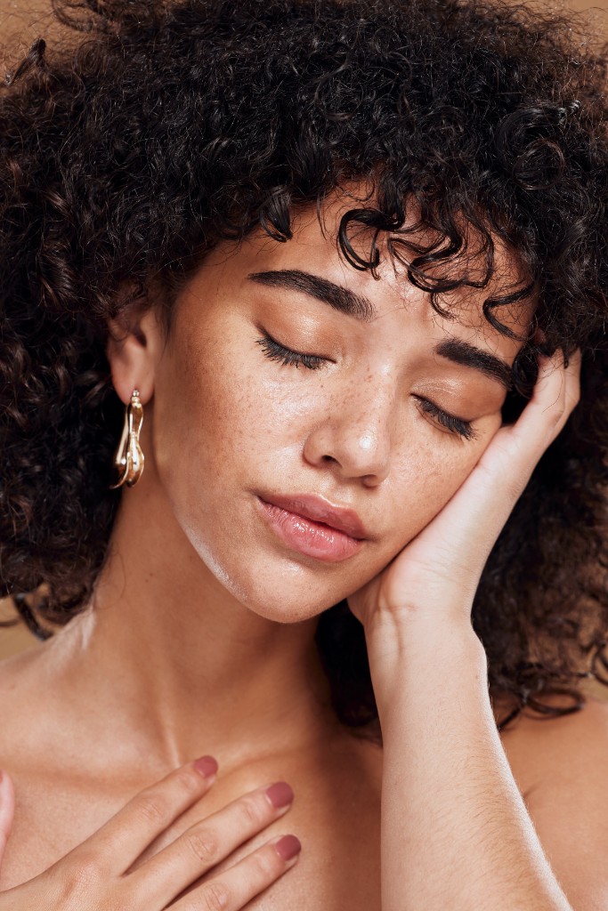 Curly-haired woman with glowing skin in warm studio light